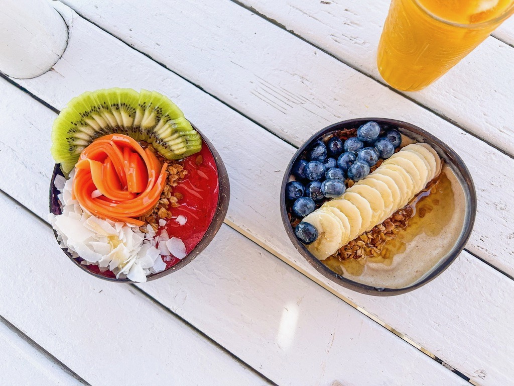 Two smoothie bowls from Nalu Bowls Ericeira, one has papaya and kiwi on top and the other has blueberries and bananas on top