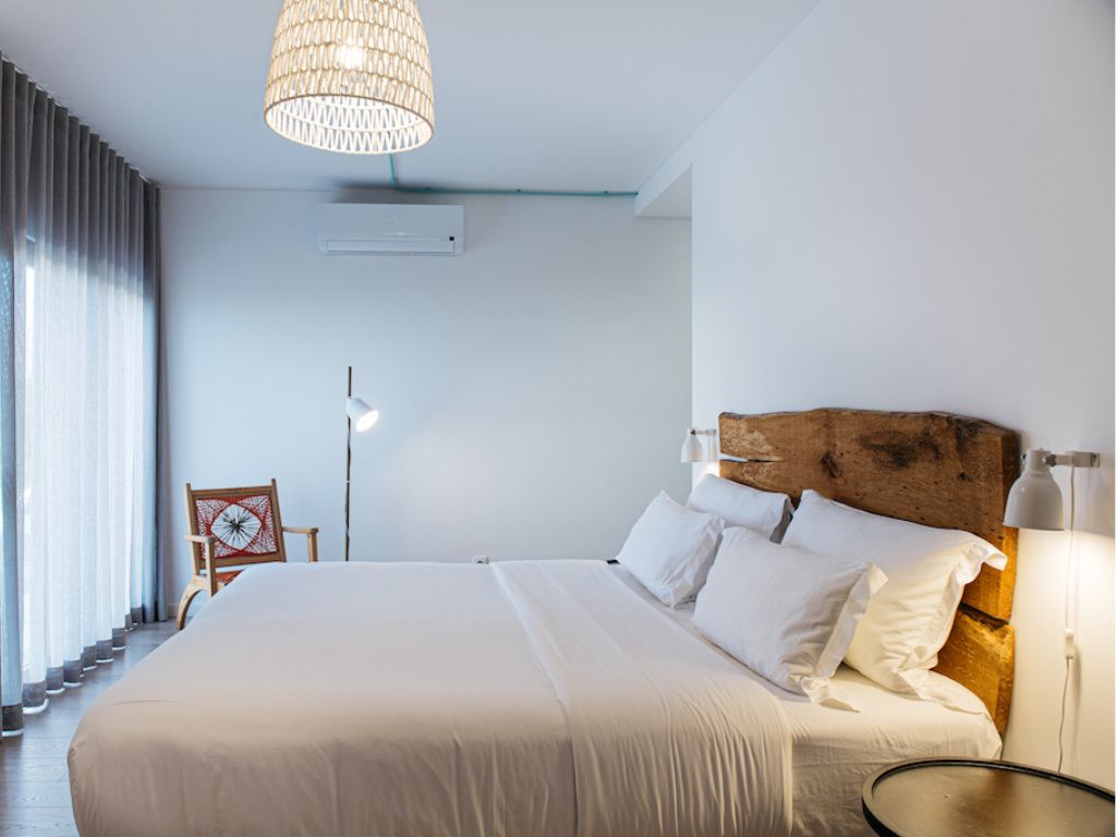 A crisp, elegant room at You and the Sea Hotel. There's a large bed with a wooden headboard, white sheets, and an artsy chair in the background.