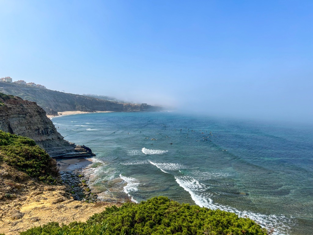 Surfers in the water near Ribeira D'Ilhas. There's fog in the background and lot of surfers in the water.
