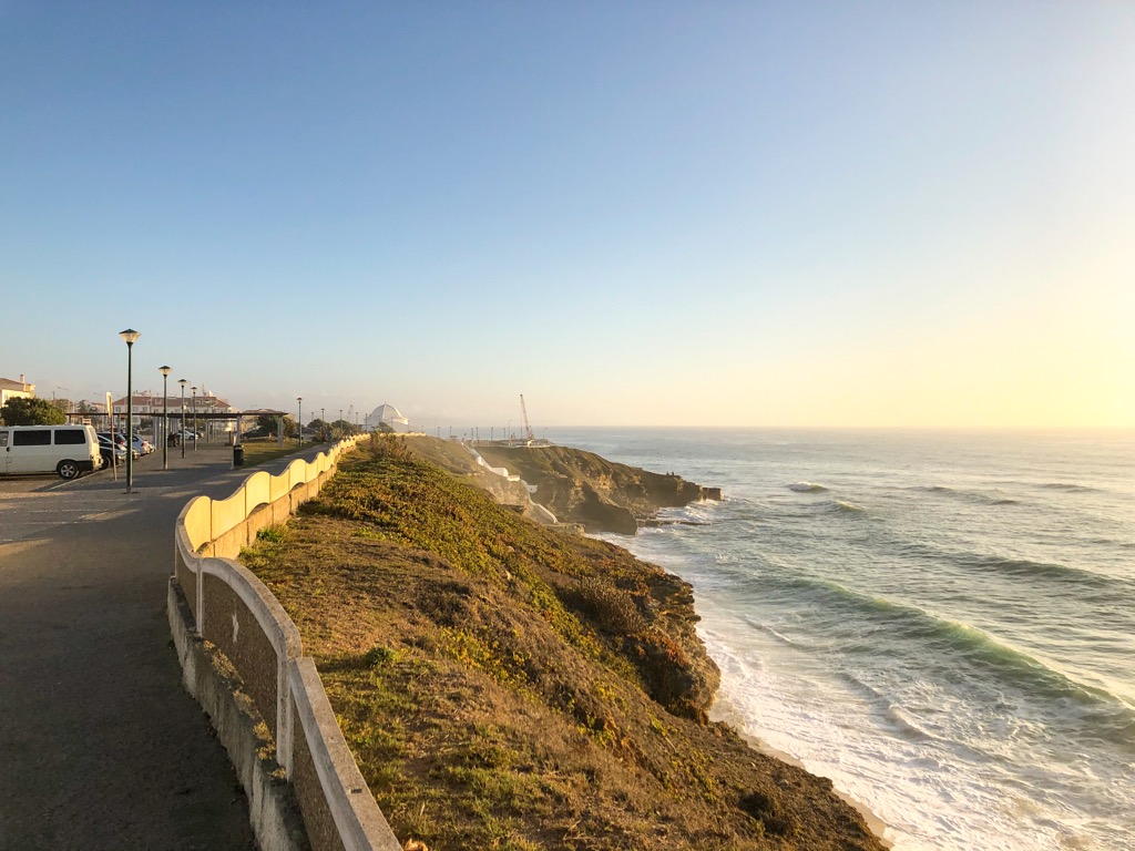 Praia de São Sebastião walkway in the late afternoon. The cliffs are grassy and the water has some light waves