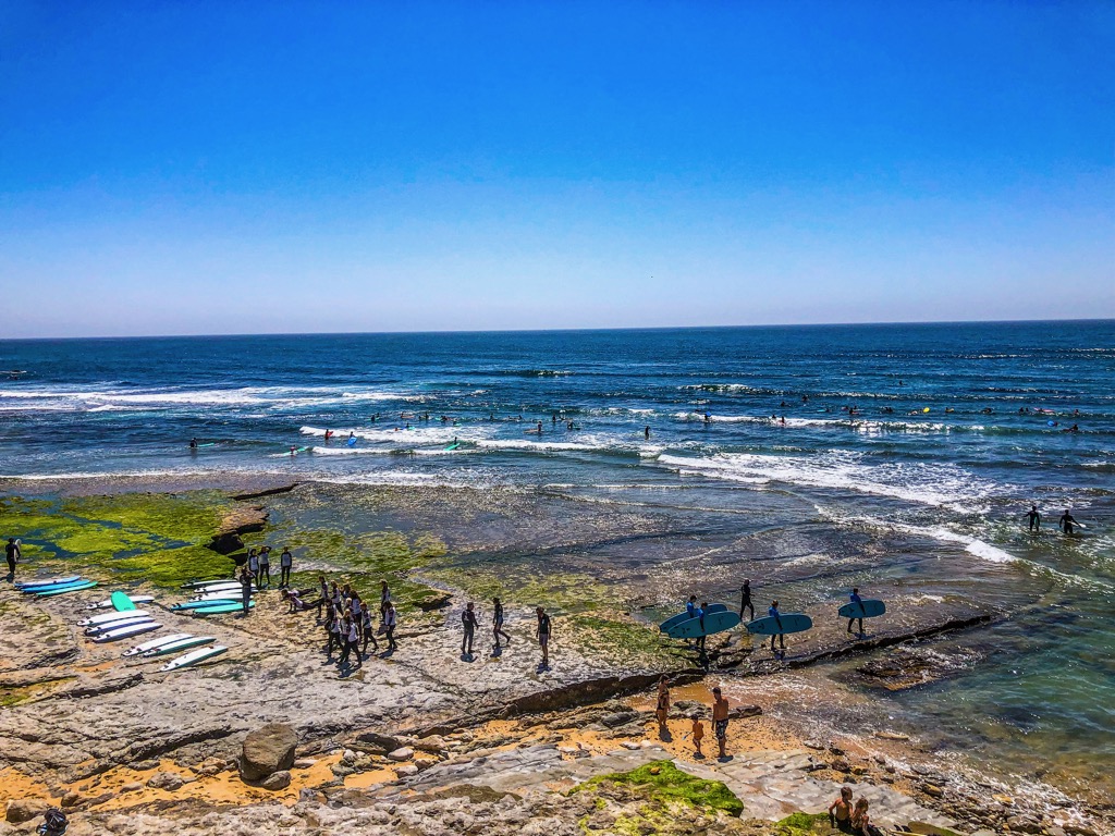Surfboards lining the beach at Praia do Matadouro while people walk out into the surf