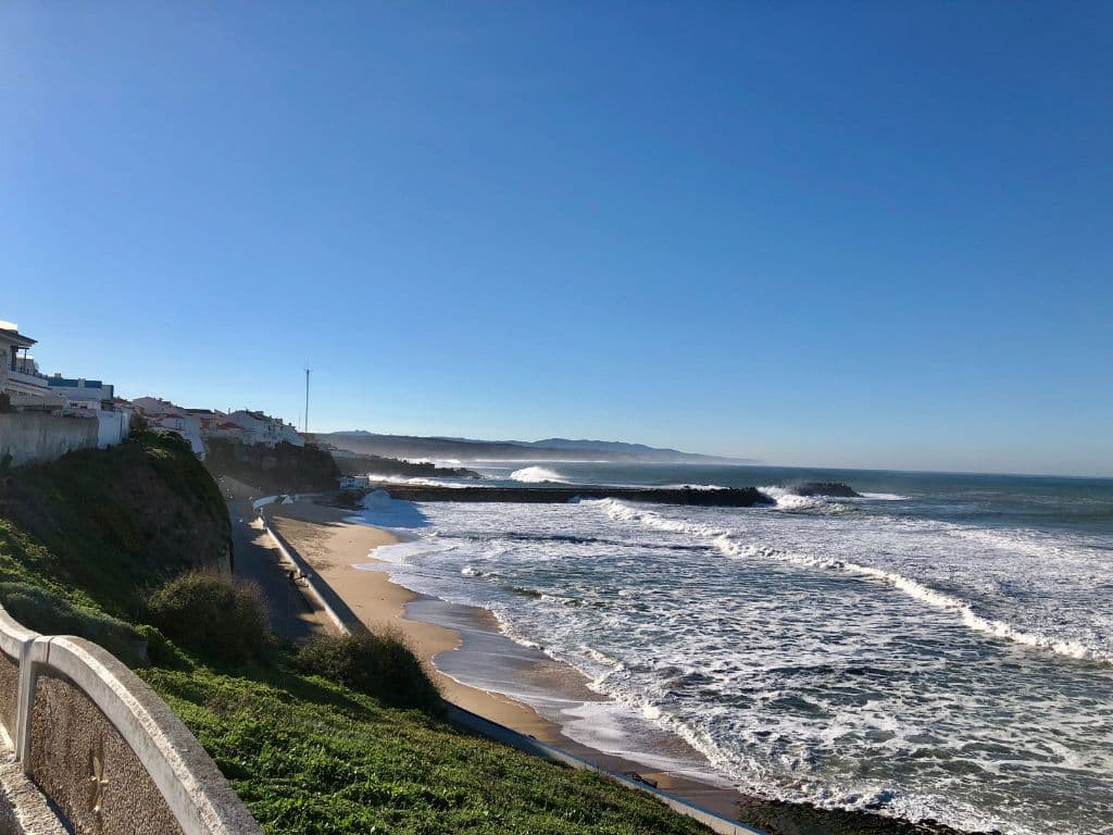 Praia de Norte at sunrise. The waves are big against the sand and you can see the town in the background.